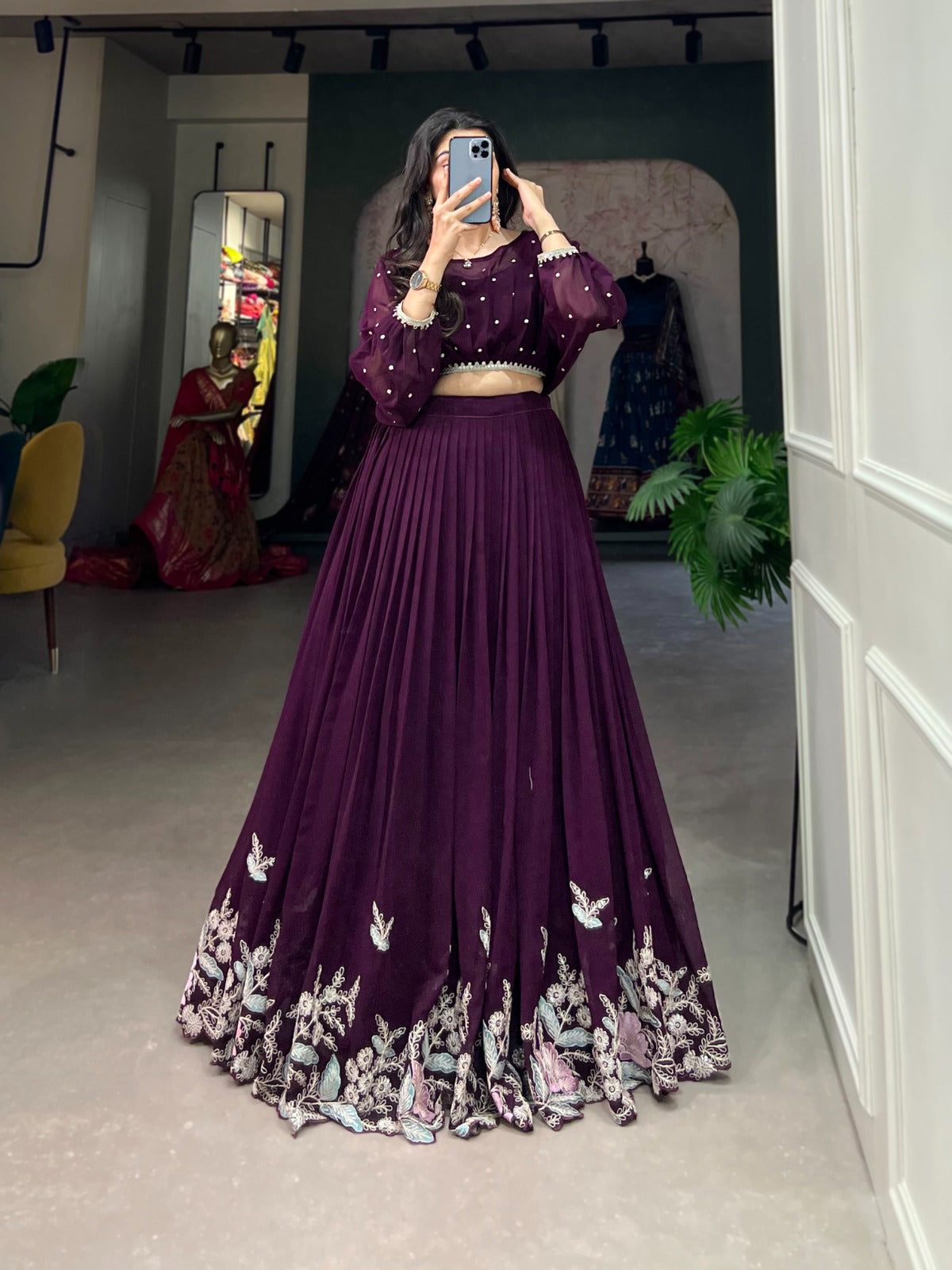 Person wearing a purple embroidered outfit in a room with mirrors and plants.
