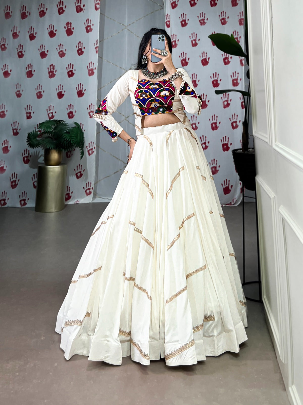 Person wearing a traditional outfit with a white skirt and multicolored top in a room.