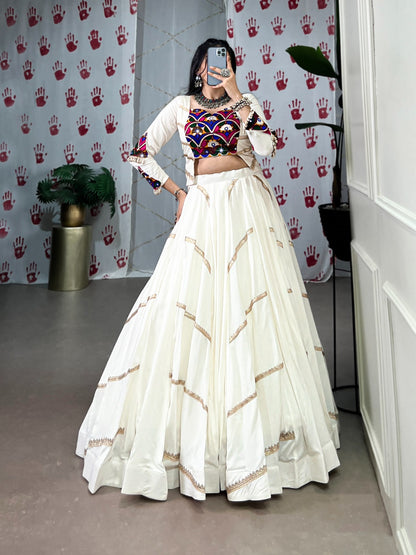 Person wearing a traditional outfit with a white skirt and multicolored top in a room.