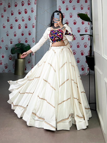 Woman in a white traditional outfit with colorful top in a room with decorative wall paper.
