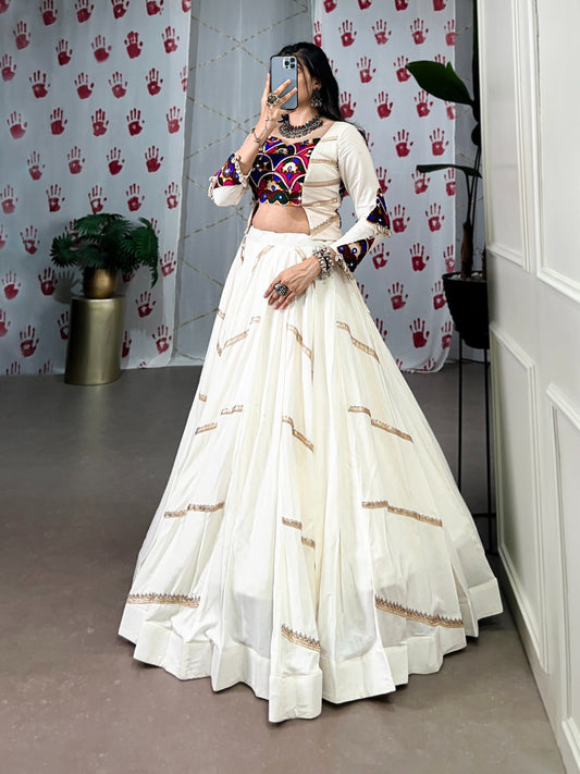 A woman in a flowing white cstands against a wall, emphasizing her elegant style and the dress's design