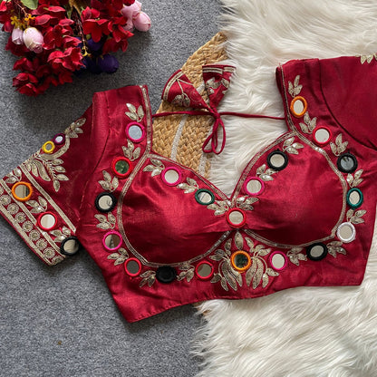 Red embroidered blouse with colorful buttons on a textured surface with flowers.