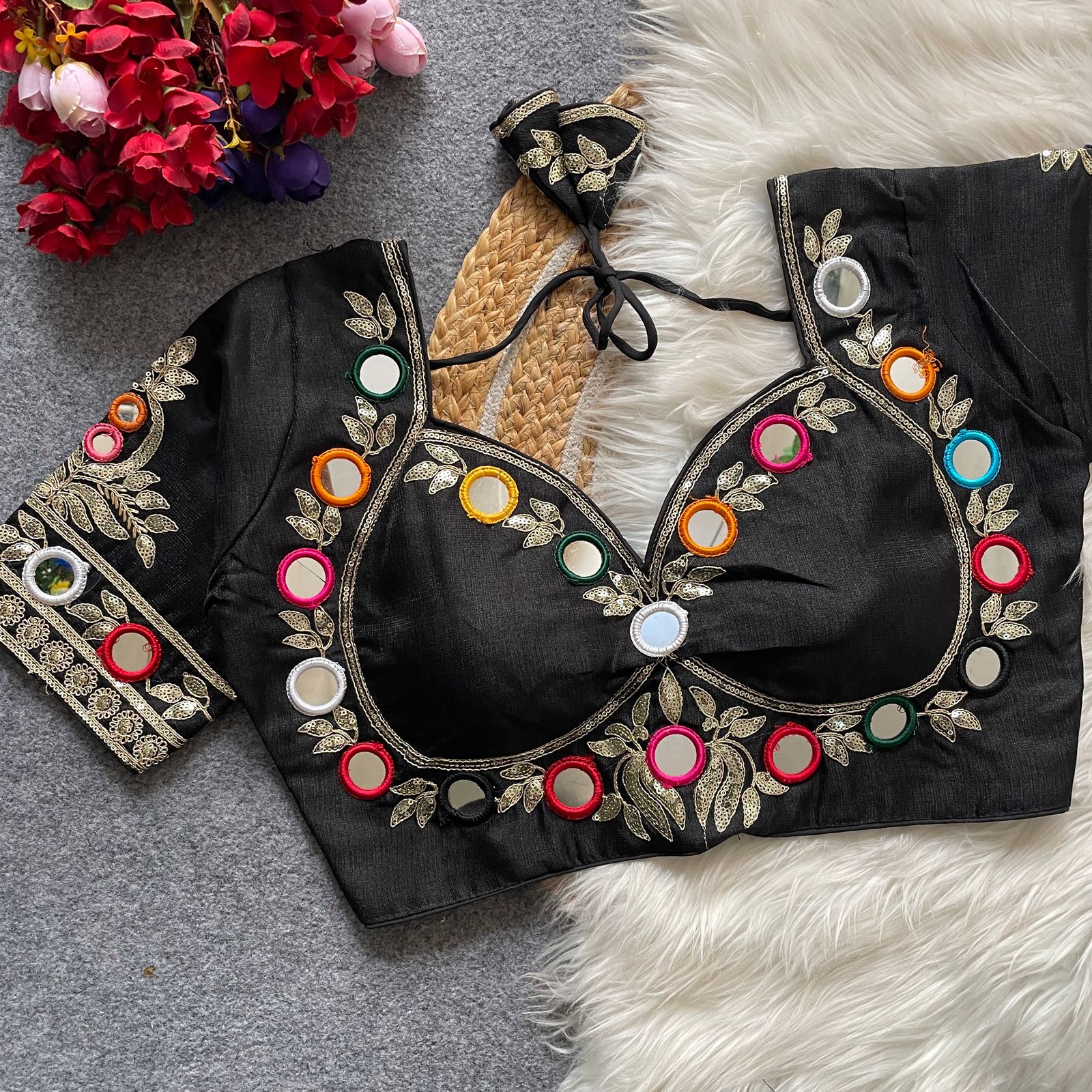 Black embroidered blouse with colorful embellishments on a textured surface with flowers.