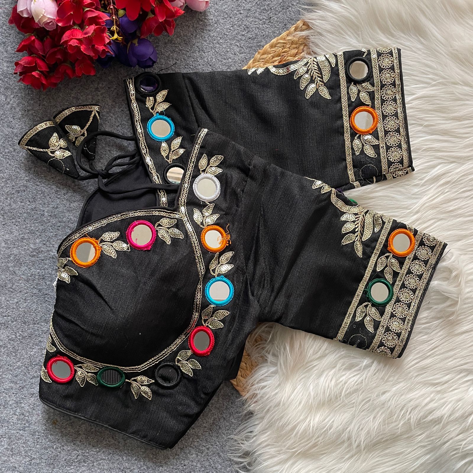 Black blouse with colorful mirror work on a textured surface with flowers