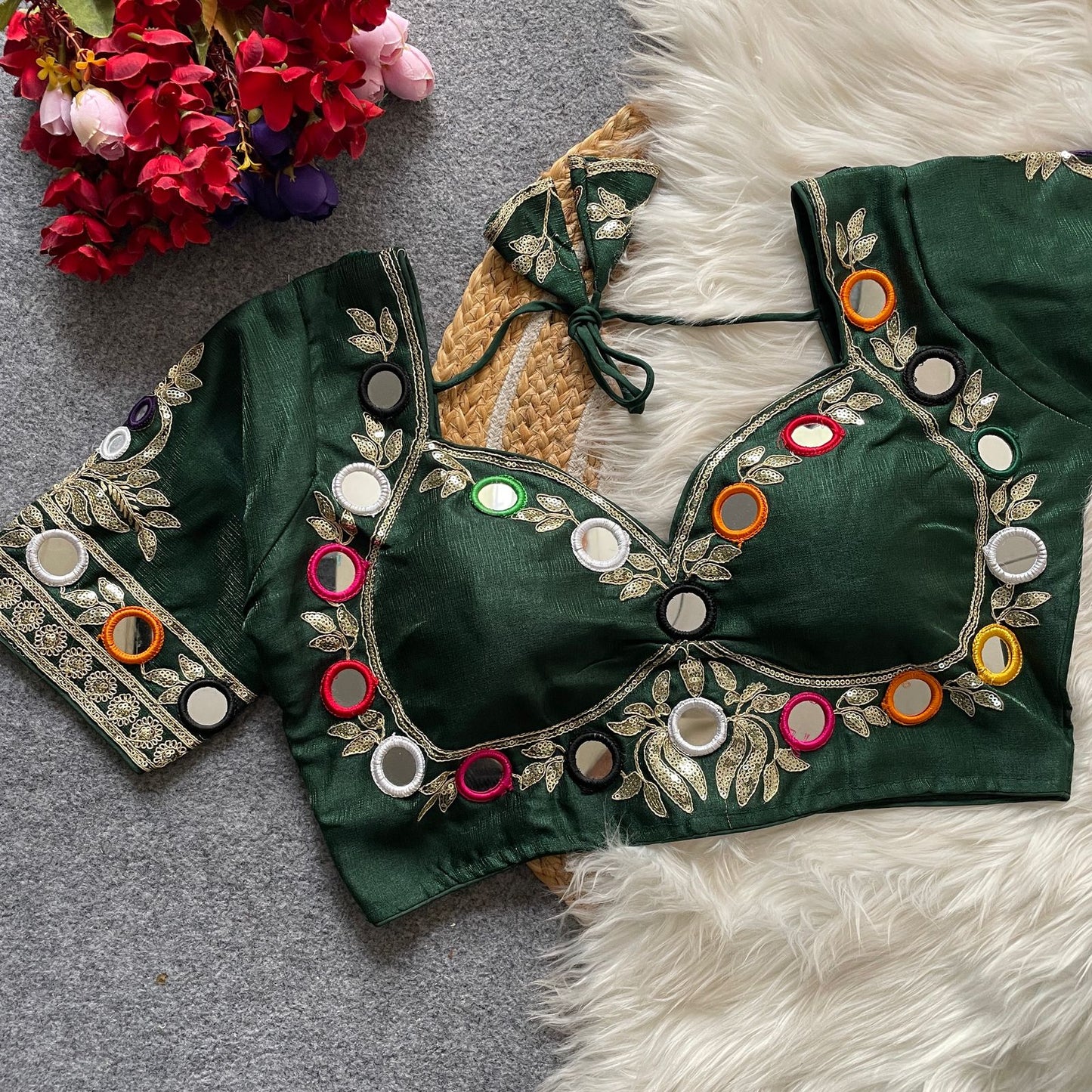 green embroidered blouse with colorful buttons on a textured surface with flowers.