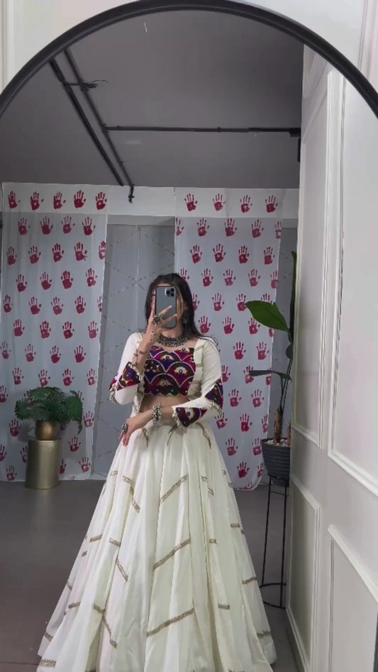 A woman in a flowing white cstands against a wall, emphasizing her elegant style and the dress's design